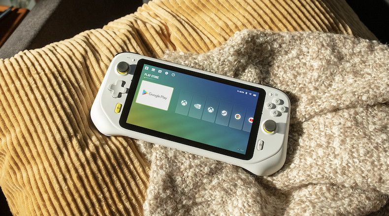 A white Logitech G Cloud handheld gaming device sits on a pillow and blanket