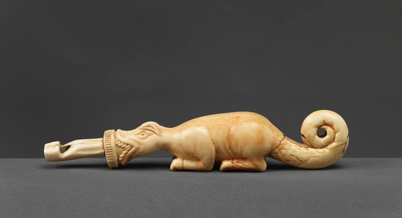 An ivory whistle carved to look like a reptile of some sort with the mouthpiece of the whistle sticking out of its jaws