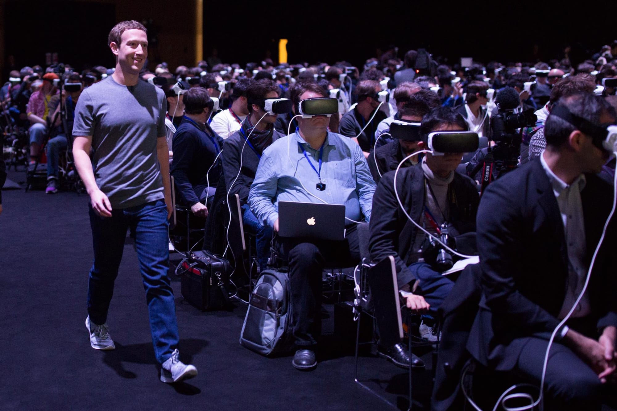 Photo of Mark Zuckerberg at a Facebook event, walking down the aisle unnoticed by the audience because they are all wearing Oculus Gear VR headsets.