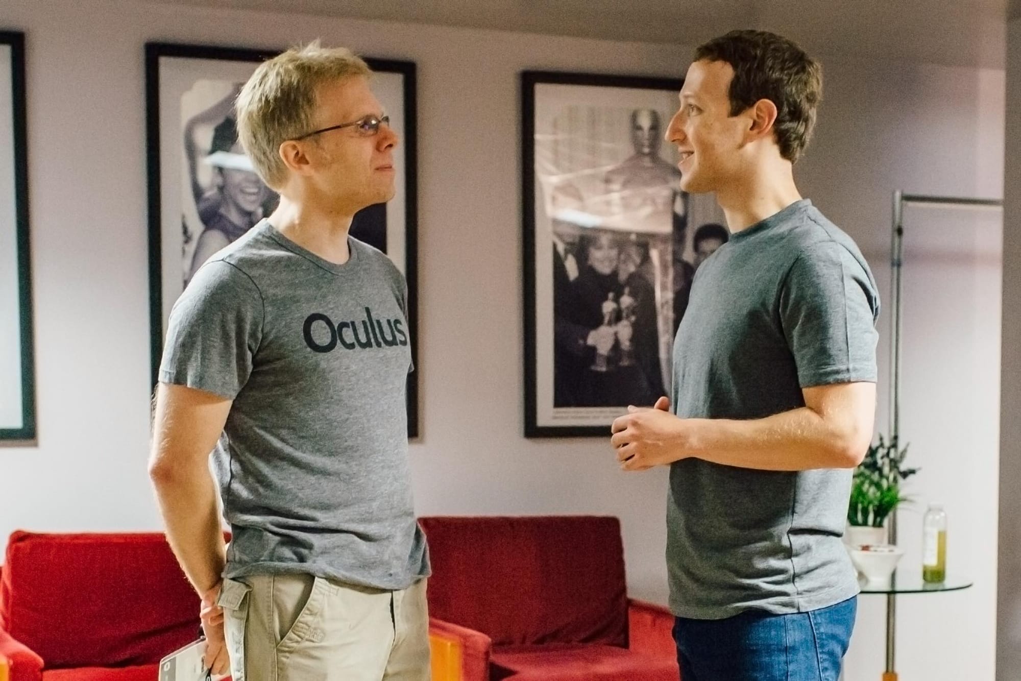 Picture of John Carmack in a gray Oculus T-shirt and Mark Zuckerberg in an unbranded gray T-shirt. They are looking at each other with Carmack tight-lipped and Zuckerberg maybe sort of smiling?