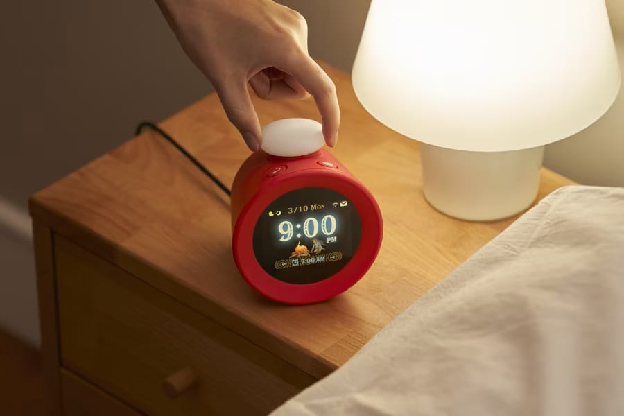 Alarmo product shot showing the clock on a bedside nightstand with a hand reaching down to touch it.